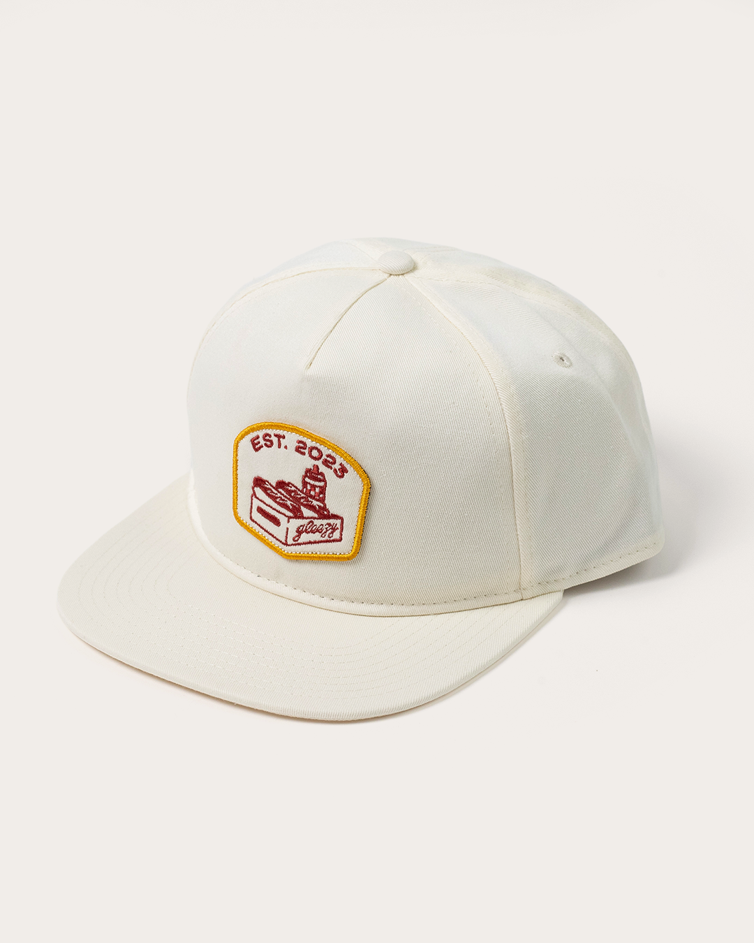 Cream snapback hat with an embroidered patch of the Gleezy hot dog box logo and 'Est. 2023'