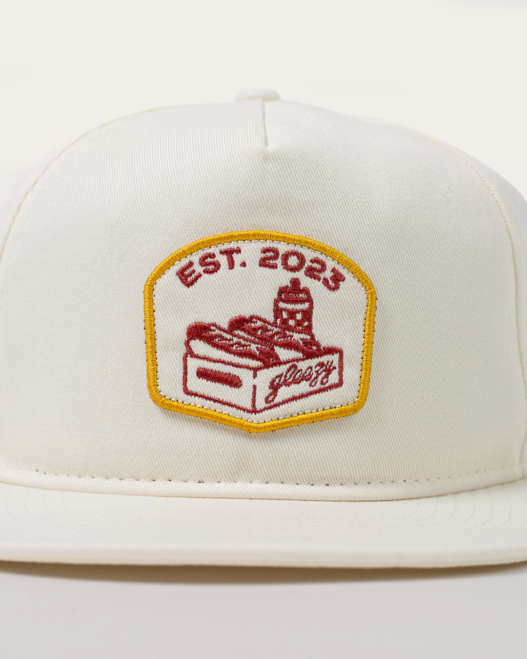 Close-up of the embroidered Gleezy hot dog box patch on the cream hat