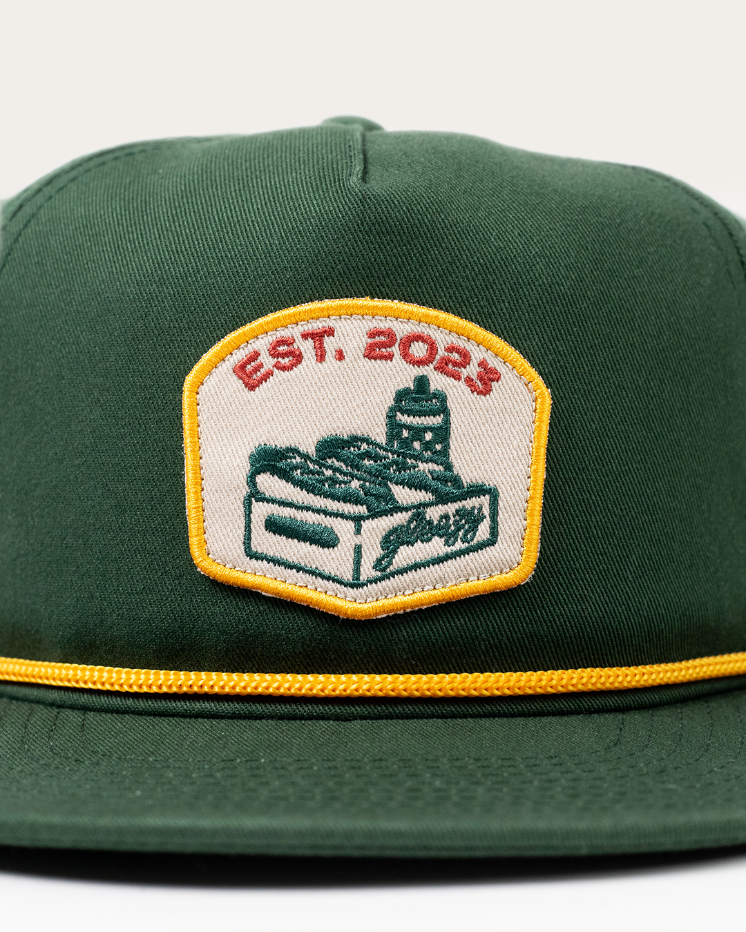 Close-up of the embroidered Gleezy hot dog box patch on the green rope snapback hat