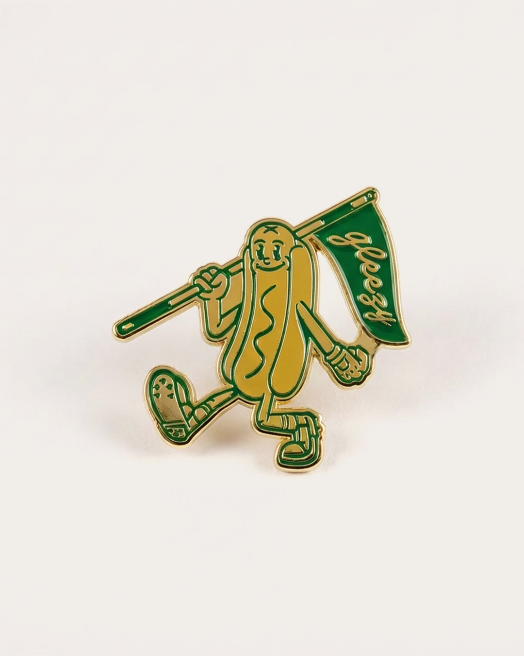 Green and gold pin with a design of a hot dog figure holding a flag on a white background