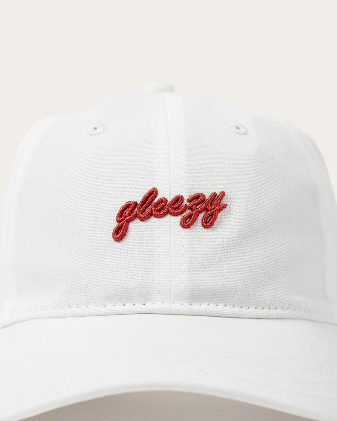 Close-up of the red Gleezy script logo embroidered on the white dad hat