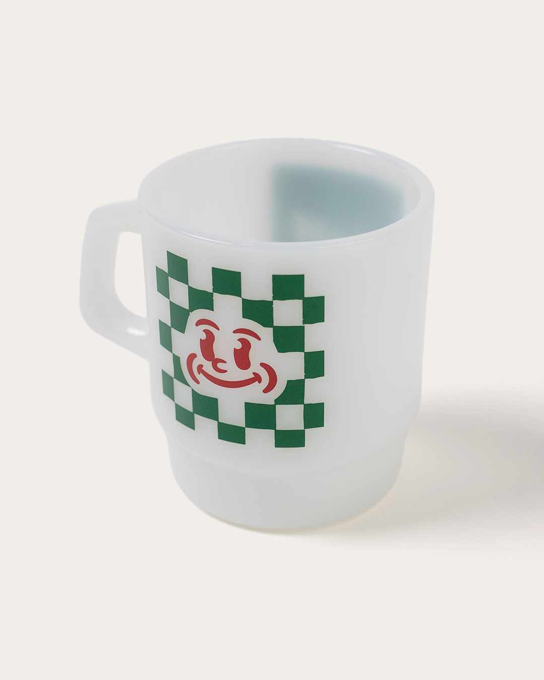 White mug with green checkered pattern and red logo on a white background