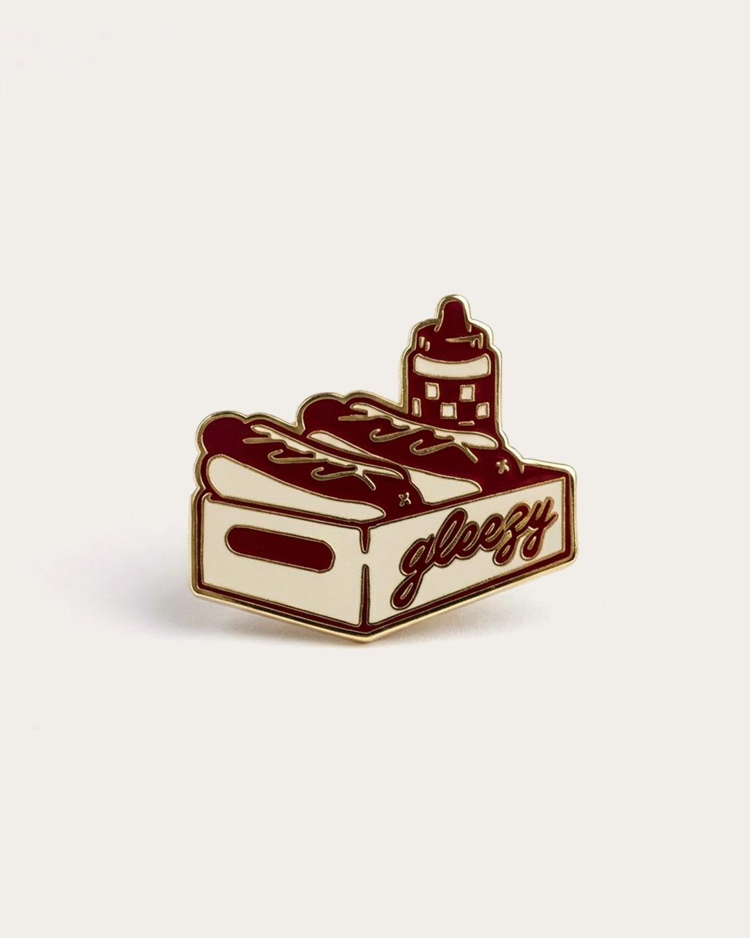 Enamel pin of a food tray with 'gleezy' branding, two hot dogs and a sauce bottle on a beige background