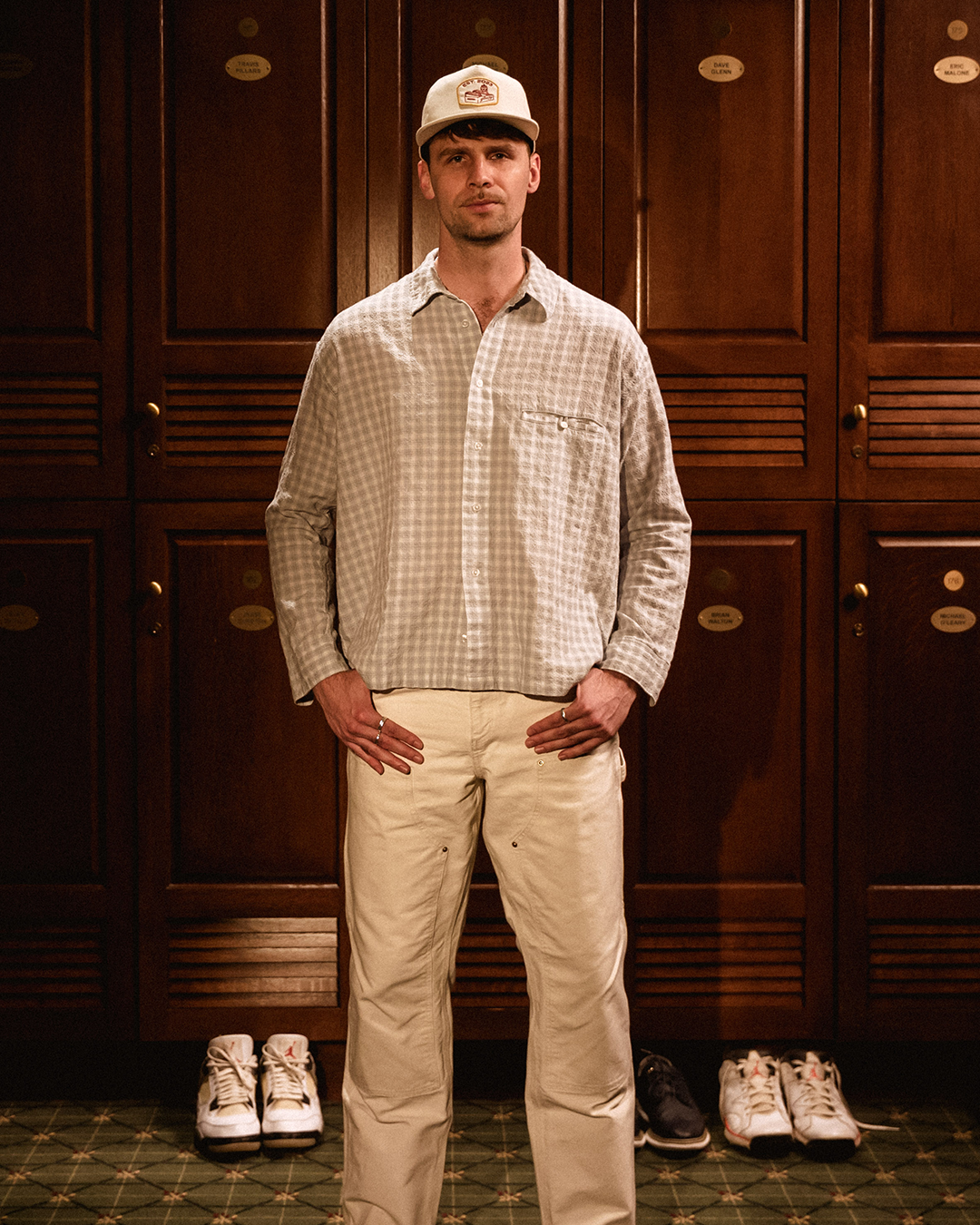 Man in a locker room wearing the cream Gleezy hat with a gingham shirt and tan pants